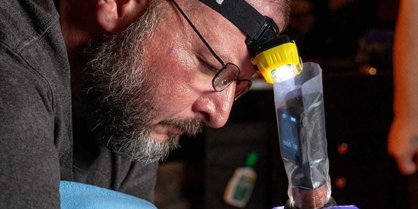 Lucas Cummins tattooing — headlamp on, machine in hand