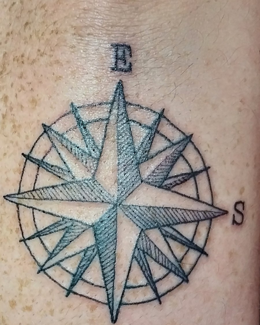 Black and grey compass rose tattoo with fine hatching, forearm